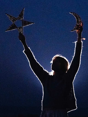 Person holding up a star and a crescent moon against a dark blue background