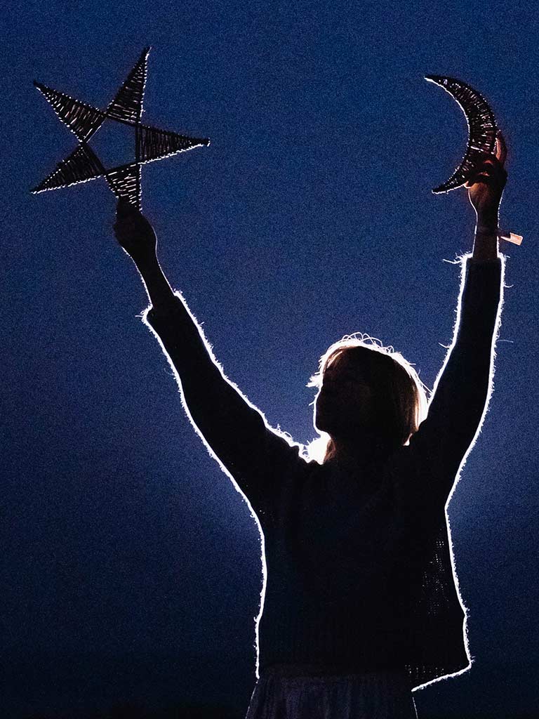 Person holding up a star and a crescent moon against a dark blue background