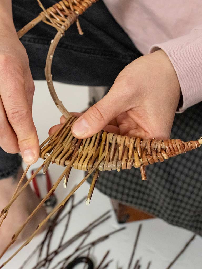 Person weaving a crescent moon out of willow.